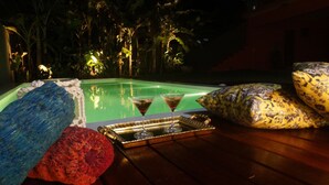 Escena junto a la piscina con una mesa de vidrio, dos copas de martini, una bandeja y un cuenco decorativo.