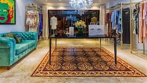 Un interior lujoso con un sofá de color turquesa suave, un tapete estampado, una araña y una tienda de ropa al fondo.