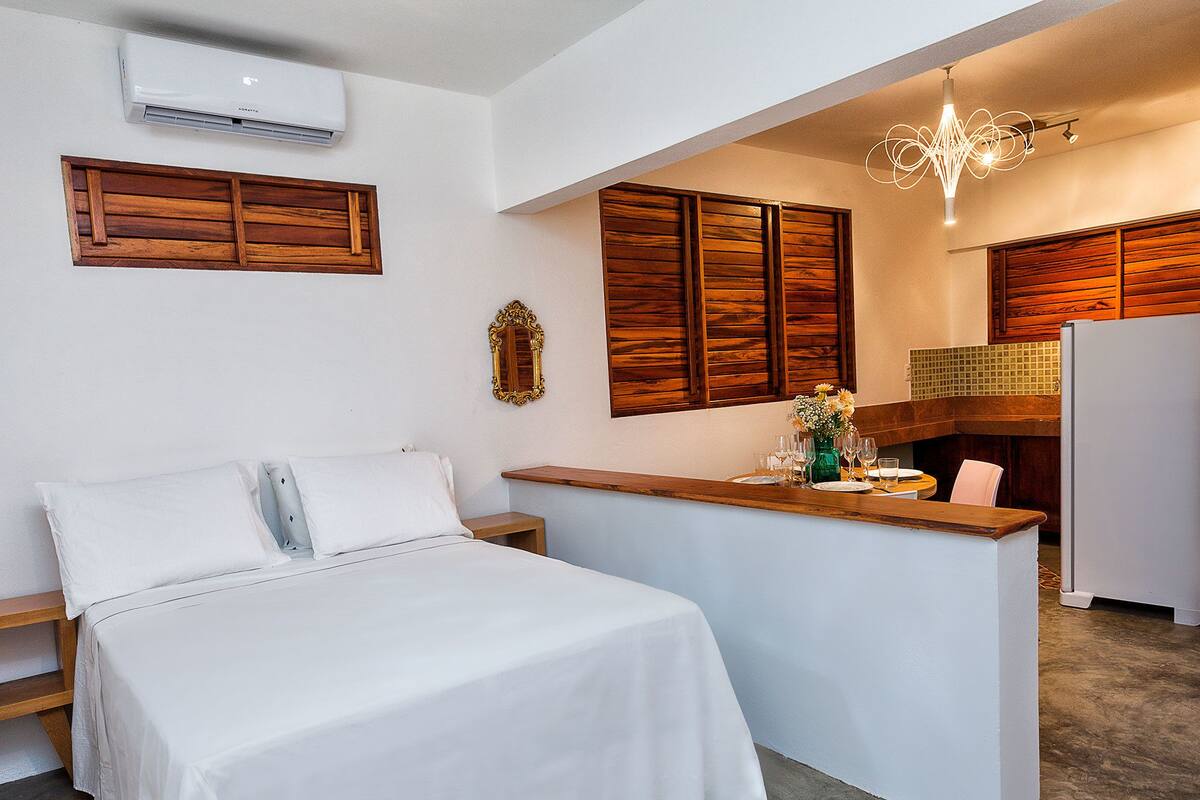 Et kompakt hotelværelse med seng, et lille bord med en vase og et tekøkken.