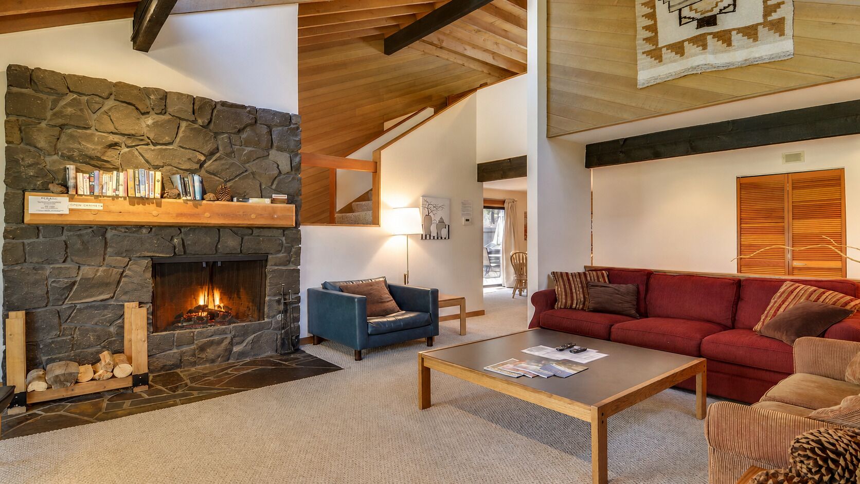 A cozy living room with a stone fireplace, a blue armchair, a red sofa, and a coffee table.