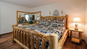 A wooden-framed bed with a checkered bedspread, a bedside lamp, and a mirror on the wall.