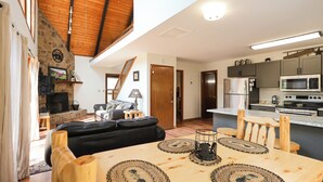 A spacious living area with a fireplace, a dining table with placemats, a kitchen with modern appliances, and a staircase leading to an upper level.