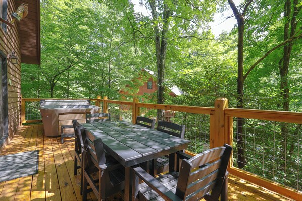 A wooden deck with a table and chairs, surrounded by a wooden railing and a view of a forest.