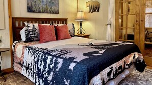 A bedroom with a wooden headboard, a bed with patterned bedding, a nightstand with a lamp, a wall-mounted bear decoration, and a sliding glass door closet. - Secluded cabin, great location, hot tub, and foosball! (Sevierville)