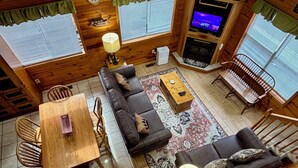 A cozy cabin interior with a wooden dining table, sofa, and a TV in the corner. - Secluded cabin, great location, hot tub, and foosball! (Sevierville)