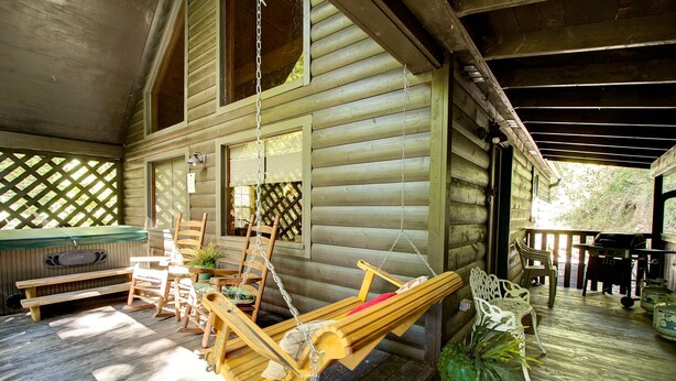A wooden cabin with a porch, a swing chair, a hot tub, and a grill. - Secluded cabin, great location, hot tub, and foosball! (Sevierville)