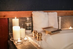 Un baño con un lavabo blanco, dos velas encendidas, una botella de jabón de lavanda y una bandeja dorada.