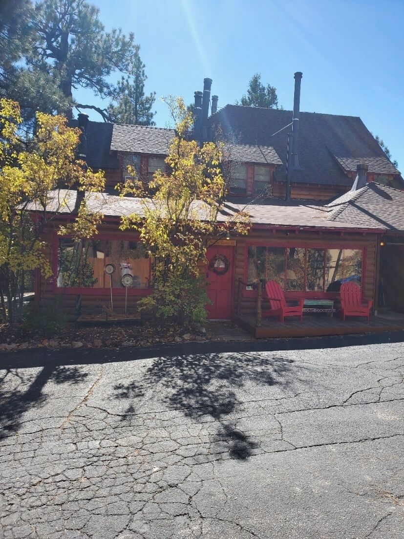 Un rustico chalet con un portico, due poltrone Adirondack rosse e un camino.