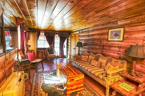 Interior acogedor de una cabaña de troncos con un sofá de madera, una mesa de centro de madera, un sillón mecedora y una chimenea.