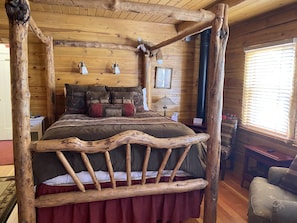 A rustic wooden room with a four-poster bed, wooden walls, and a large window with blinds. - Gold Mountain Manor Bed and Breakfast (Big Bear City)
