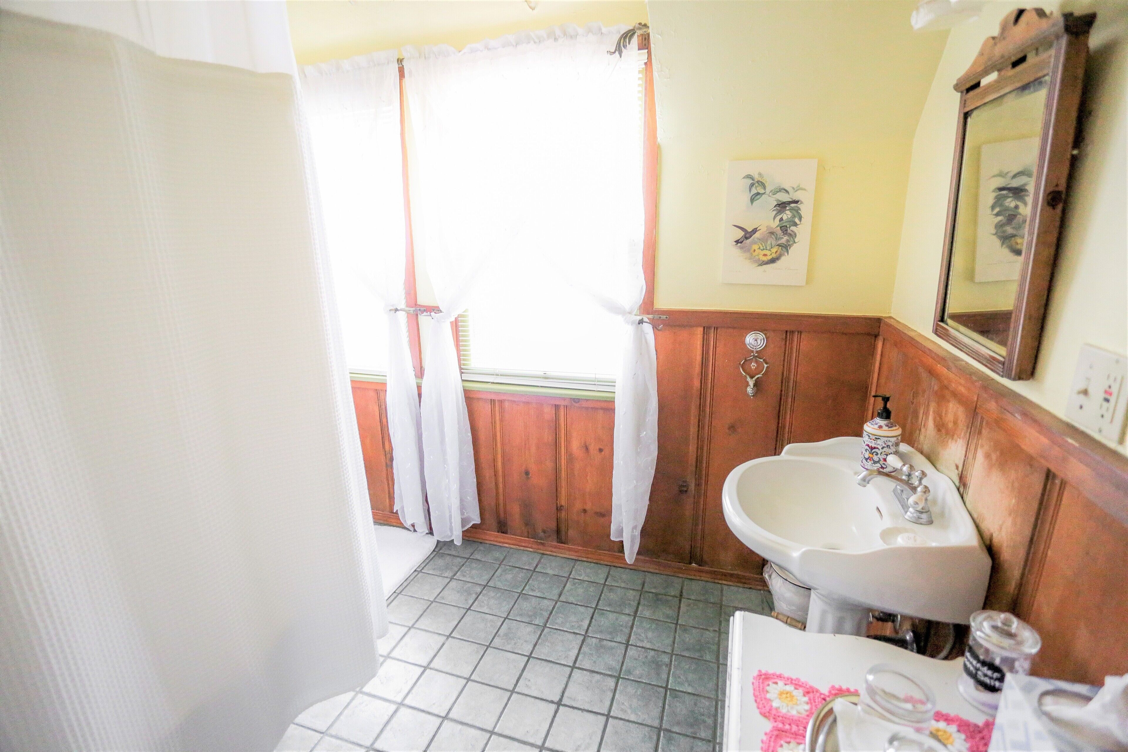 A bathroom with a sink, mirror, and a window with curtains.