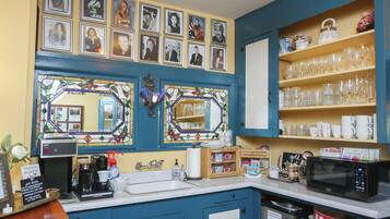 Una cocina con armarios azules, una cafetera y un microondas. Hay cuadros en la pared y estantes con vasos y tazas.
