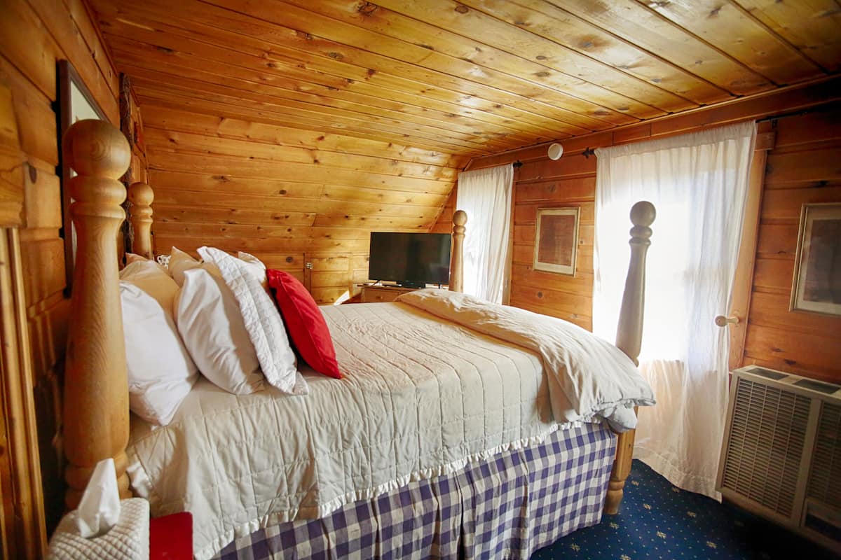 A wooden cabin bedroom with a bed, a television, and a window with curtains.