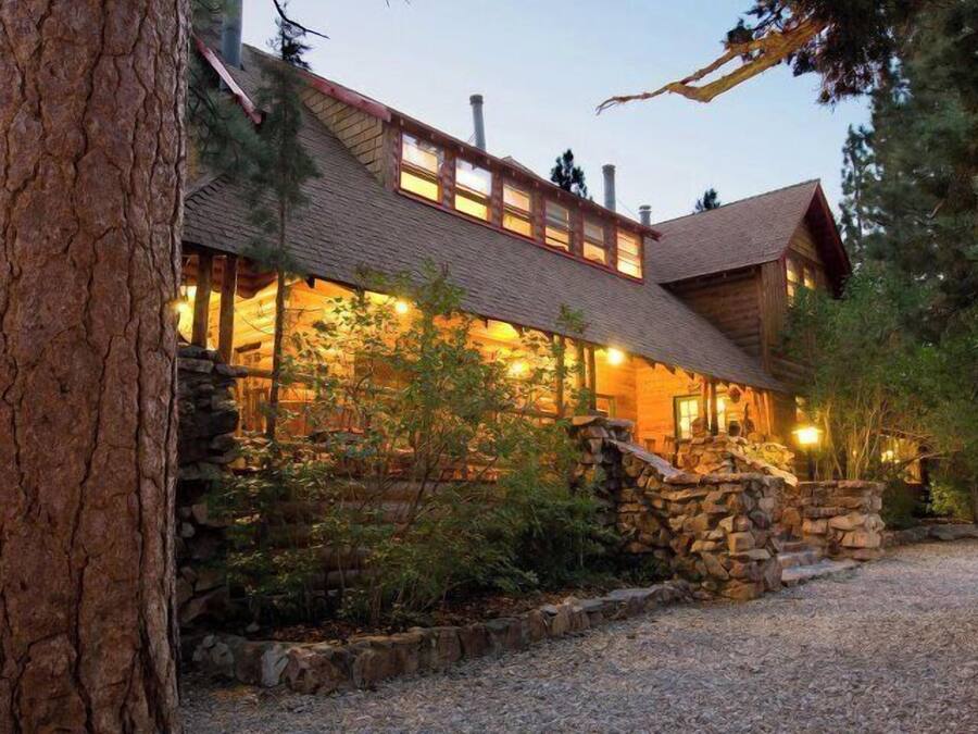 A log cabin with a stone foundation, wooden exterior, and a gravel driveway.