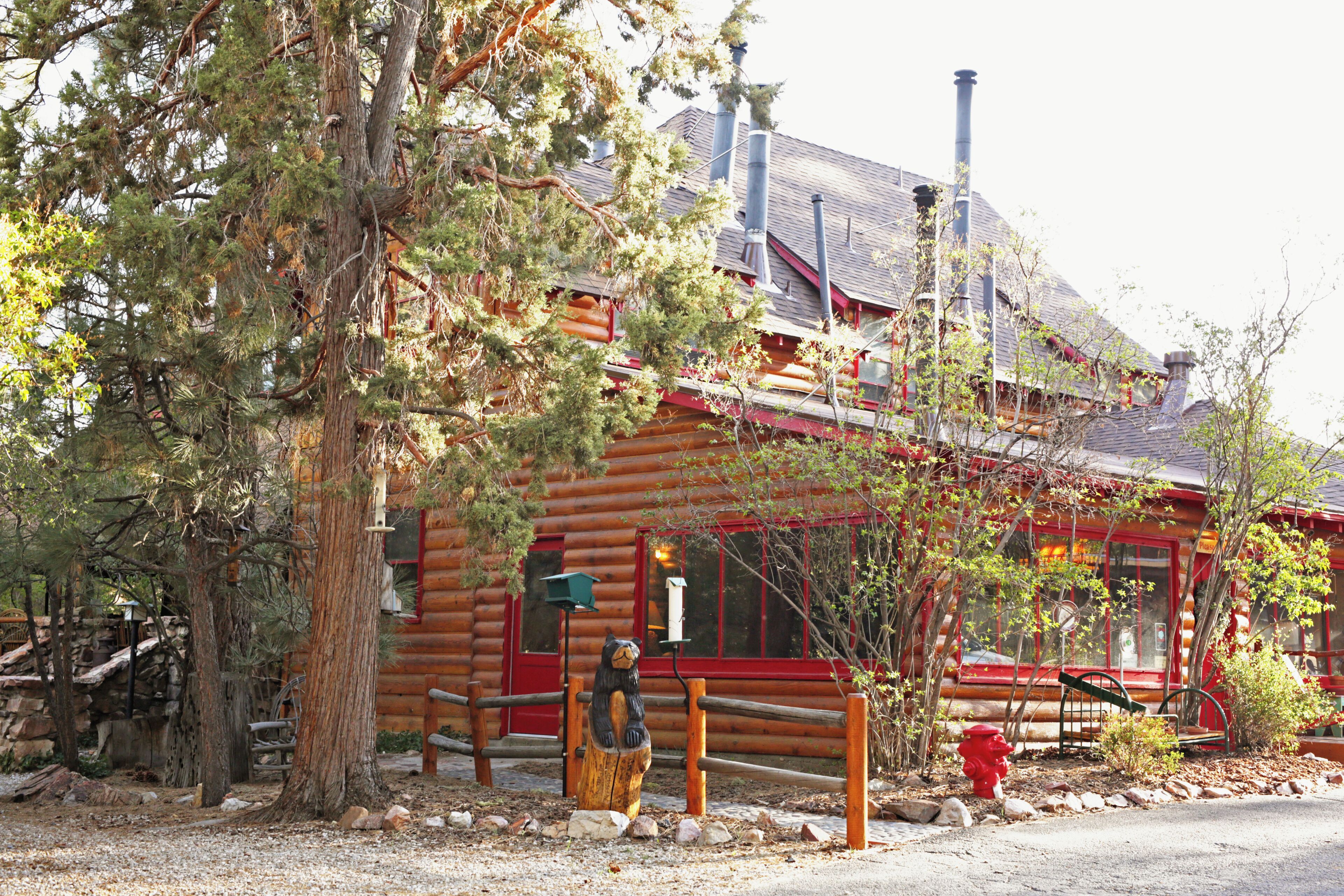 A log cabin with a chimney, a bear sculpture, and a red fire hydrant.