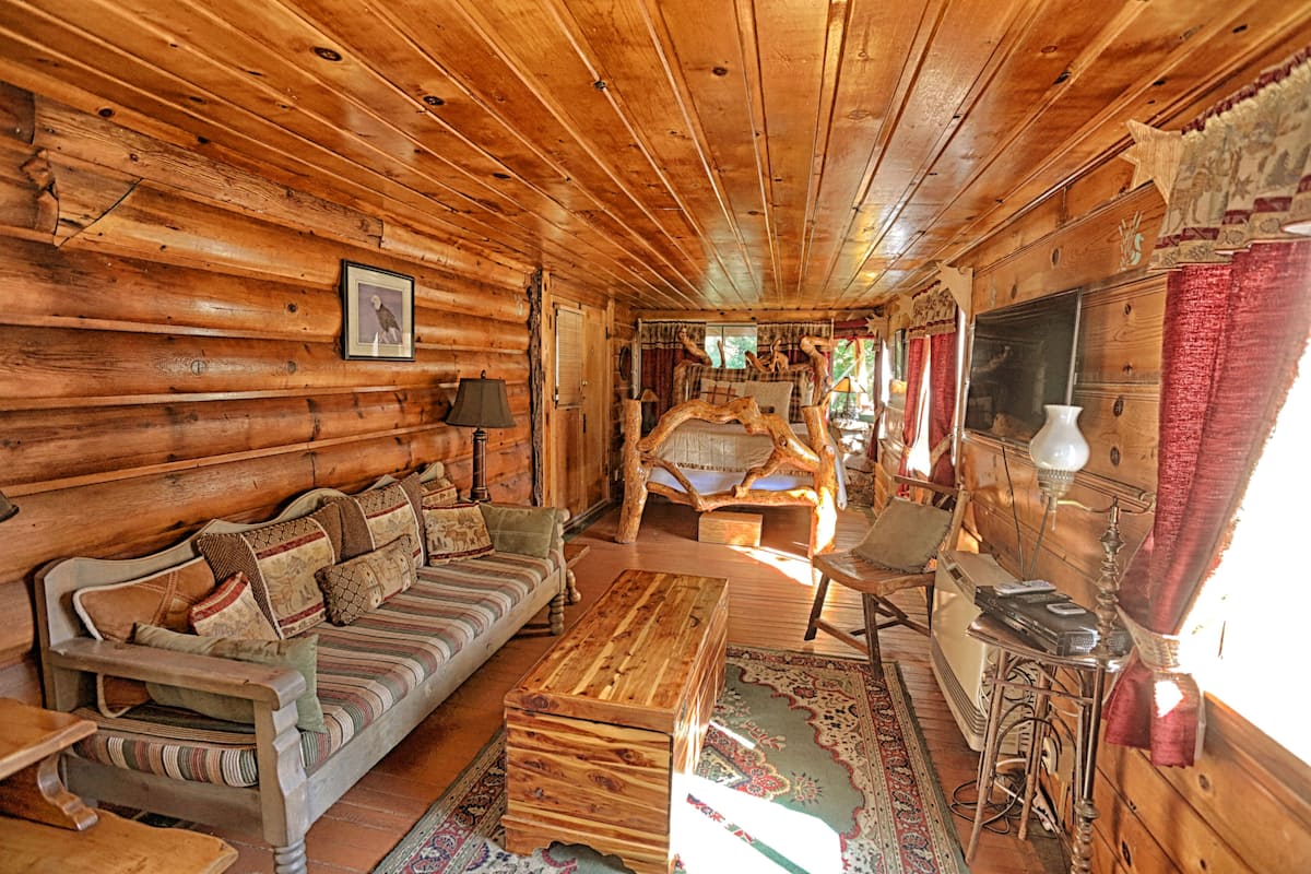 A log cabin interior with a wooden sofa, a wooden coffee table, a rocking chair, and a fireplace.
