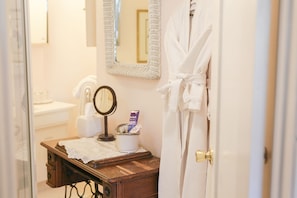 A bathroom with a wooden vanity, a mirror, a towel, and a robe hanging on the door. - Gold Mountain Manor Bed and Breakfast (Big Bear City)