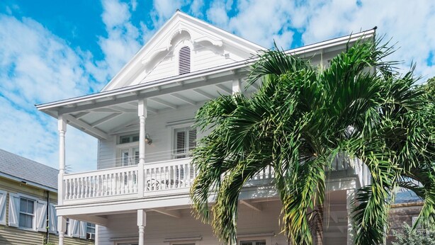 A white colonial-style building with a balcony and a palm tree in the foreground.