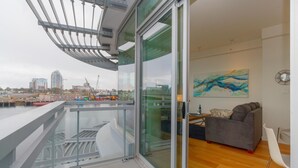 Un salon moderne avec une porte vitrée donnant sur un balcon, un canapé gris, un fauteuil blanc et un tableau accroché au mur.