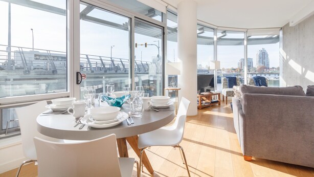 Un salon moderne avec un coin repas, de grandes fenêtres et une vue sur un pont et des immeubles.