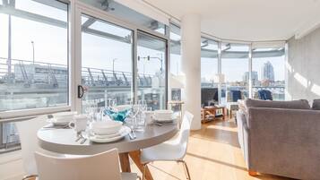 Una sala de estar moderna con comedor, ventanas amplias y vistas a un puente y edificios.