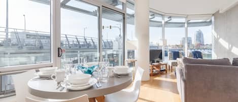 Ein modernes Wohnzimmer mit Essbereich, großen Fenstern und Blick auf eine Brücke sowie Gebäude.