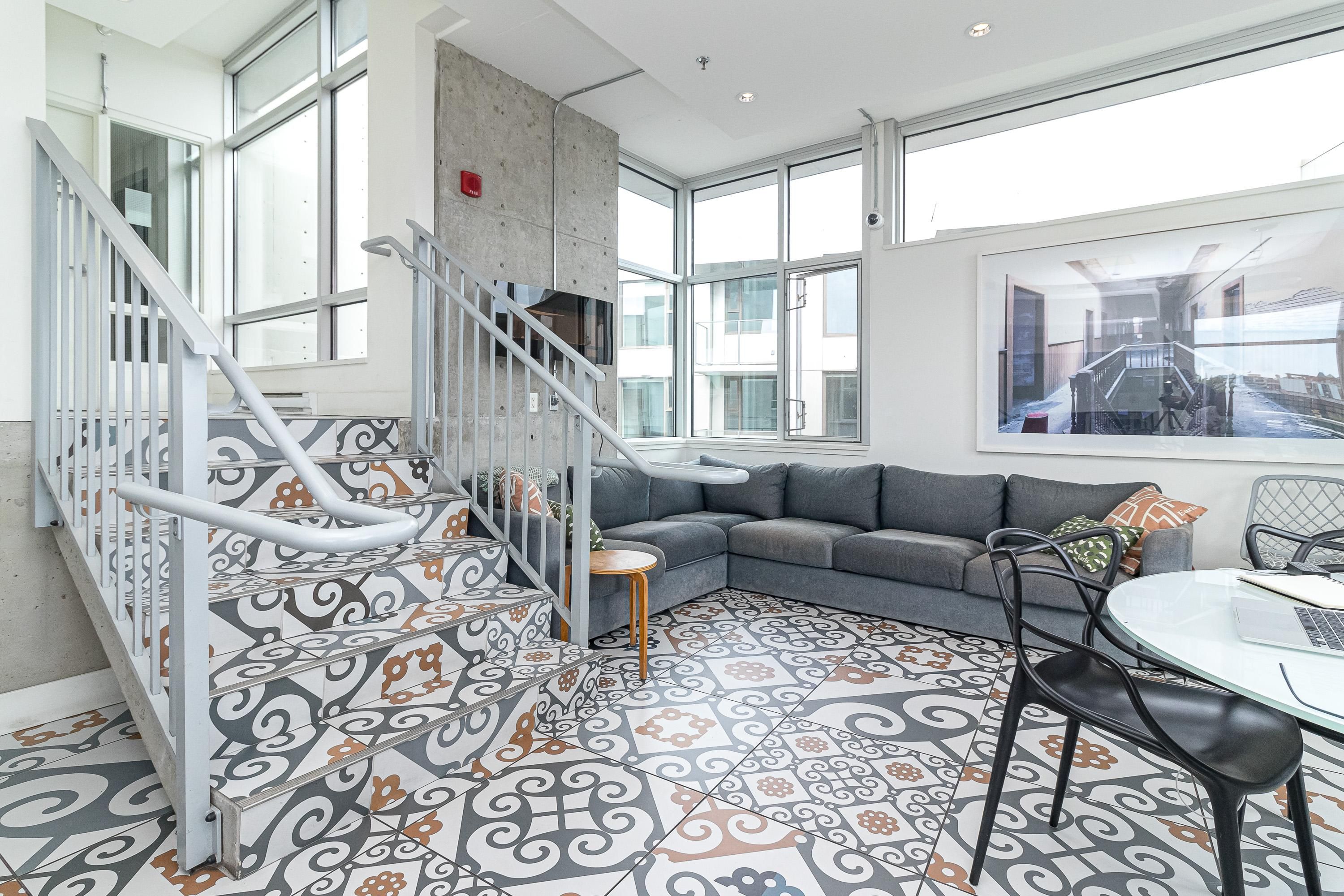A modern interior with a staircase, a gray sofa, and patterned floor tiles.