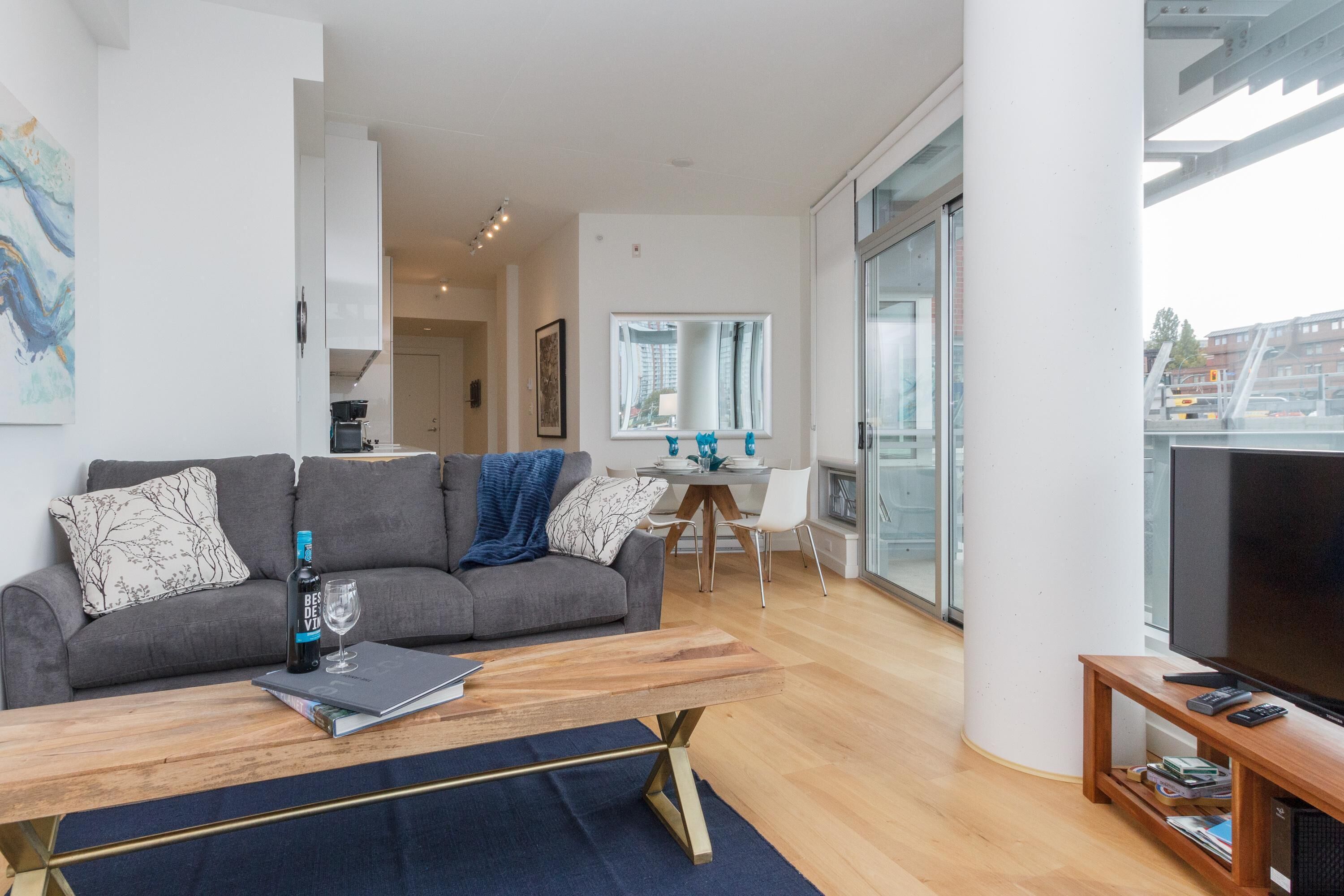 Una sala de estar moderna con un sofá gris, una mesa de centro de madera y un mueble para televisor.