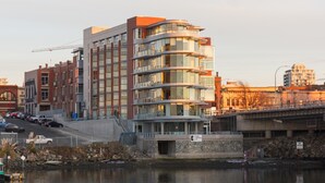 Un immeuble à plusieurs étages doté d’une architecture moderne, caractérisé par un mélange de façades en verre et en brique, et une entrée imposante avec un socle en pierre.