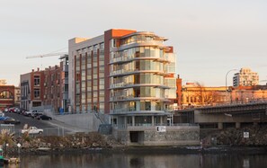 A multi-story building with a modern architectural design, featuring a mix of glass and brick facades, and a prominent entrance with a stone base. - Historic Waterside with Spectacular Johnson Bridge Views (Victoria)