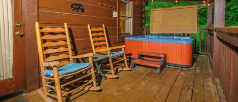 A wooden deck with rocking chairs and a hot tub.