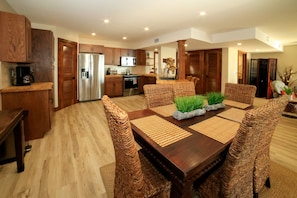 A dining area with a wooden table, wicker chairs, and a kitchen in the background. - Somewhere on the Beach a dream property all amenities included simply amazing (Key West)