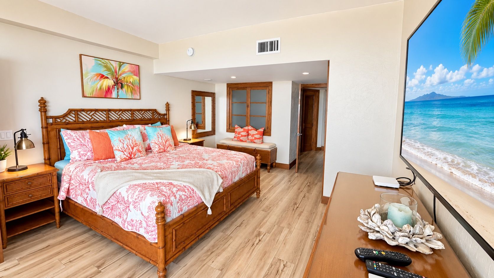 A bedroom with a bed, bedside tables, a nightstand, a window with a beach view, and a door leading to another room.