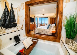 A bathroom with a bathtub, a mirror, and a view of a bedroom with a bed, a dresser, and a window overlooking the sea. - Somewhere on the Beach a dream property all amenities included simply amazing (Key West)