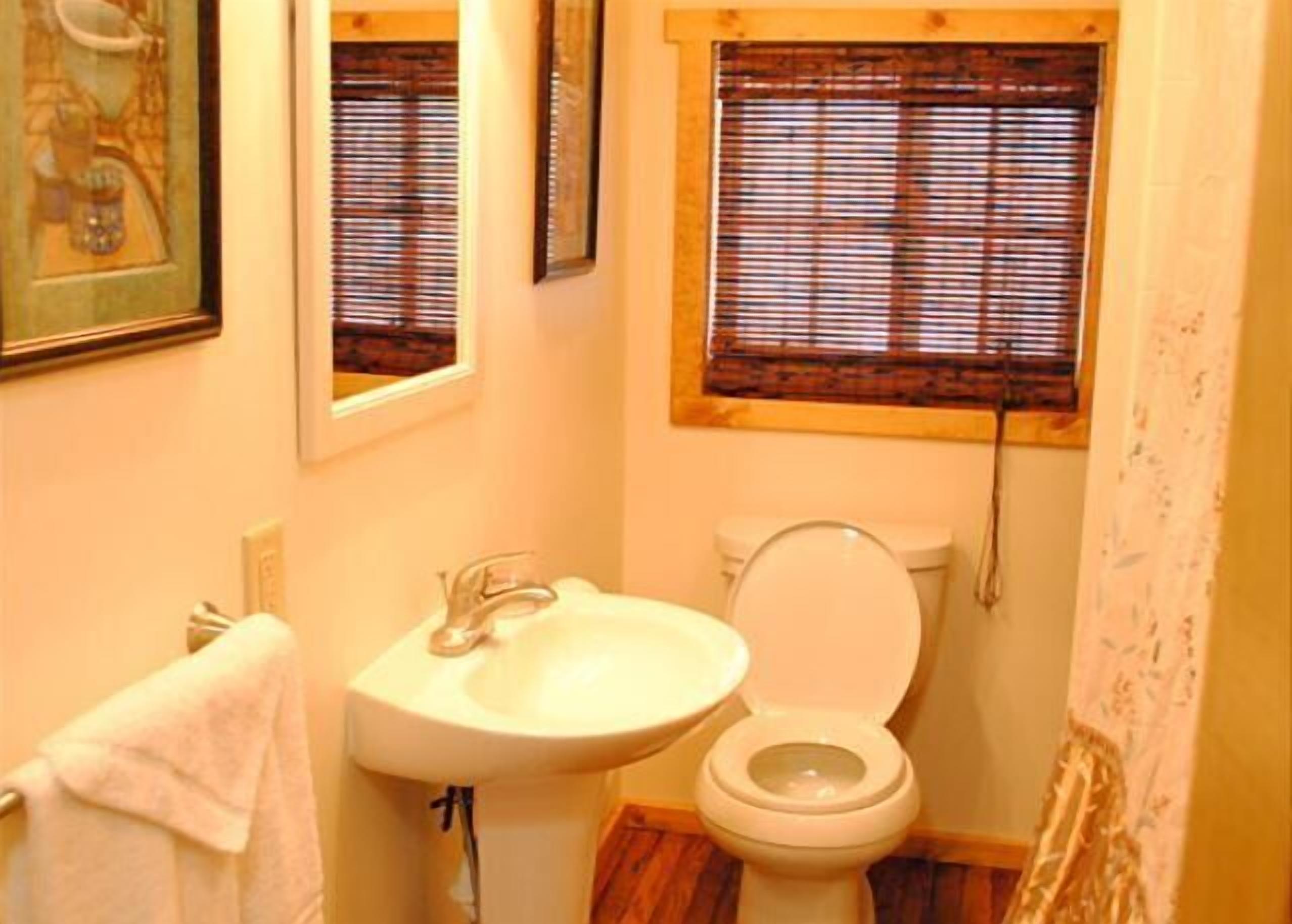 Ein kleines Badezimmer mit Waschbecken, Toilette und einem Fenster mit Jalousien.