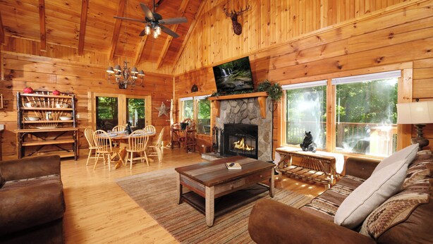 Interior de una cabaña de madera con chimenea, muebles de madera y ventanas amplias.