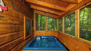 Una cabaña de madera con jacuzzi, ventanas amplias y vistas al bosque.