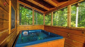 Una cabaña de madera con jacuzzi, ventanas amplias y vista al bosque.