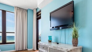 Ein Zimmer mit großem Fenster, einem flachbildfernseher an der Wand, einem Korbtisch und einem Blumentopf.