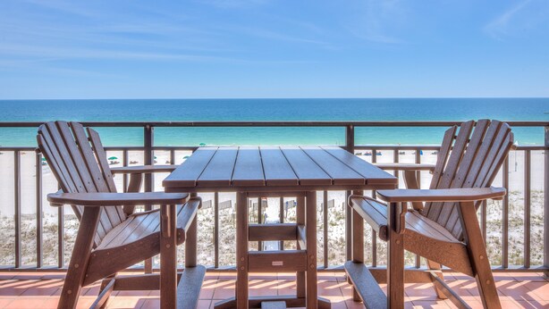 Ein Holztisch und zwei Stühle auf einem Balkon mit Blick auf einen Strand.
