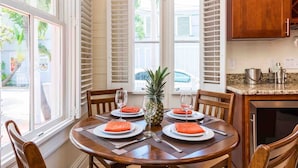 Un coin repas avec une table ronde dressée pour quatre personnes, agrémentée d’assiettes blanches, de serviettes orange et d’un ananas en guise de centre de table.