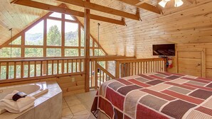 Une chambre de style cabane en bois, dotée d’une grande fenêtre, d’un ventilateur de plafond, d’une cheminée et offrant une vue sur l’extérieur.