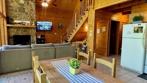 L’intérieur chaleureux d’un chalet avec une cheminée en pierre, des meubles en bois, un téléviseur et un escalier.