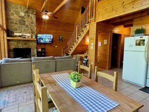 A cozy cabin interior with a stone fireplace, wooden furniture, a television, and a staircase.