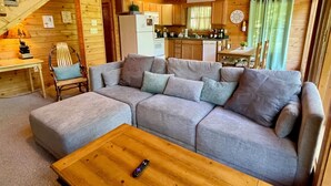 Un intérieur de chalet chaleureux avec un canapé, une table basse en bois, un coin repas et une cuisine.