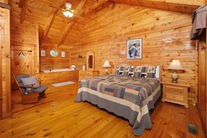 A wooden cabin bedroom with a bed, nightstands, a chair, a dresser, a vanity, and a ceiling fan.