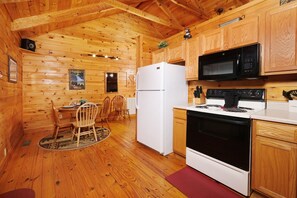 A wooden cabin interior with a kitchen area featuring a refrigerator, microwave, stove, and wooden cabinets.