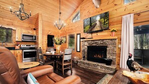 A log cabin interior with a dining area, fireplace, and kitchen. - Outdoor TV on screened in porch, hot tub, arcade game, ticket to Dollywood (Sevierville)