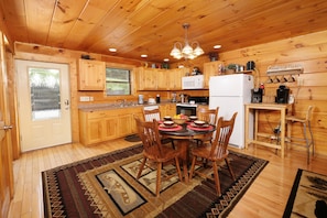 A wooden cabin kitchen with a dining table, chairs, a refrigerator, and a coffee station.