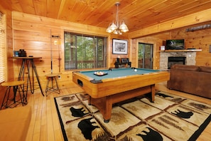 A wooden interior with a pool table, a fireplace, and a television.